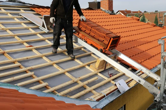 Chantier de couverture en extérieur avec ouvrier couvreur installant des tuiles terre cuite sur toiture résidentielle