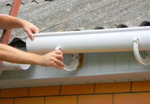 Scène extérieure de pose de gouttière blanche en PVC sur toiture