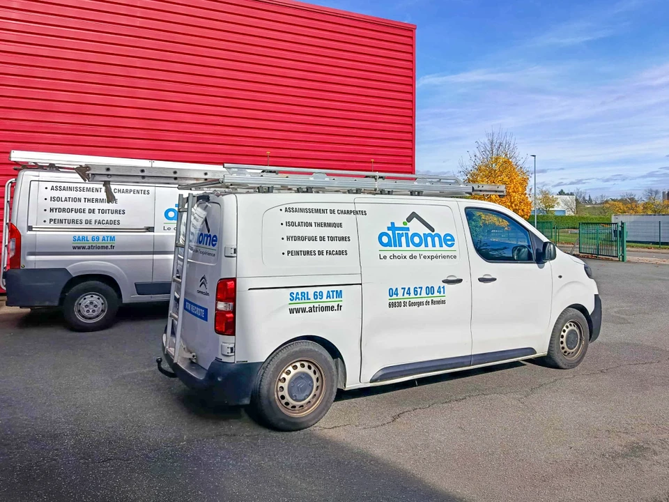 Ouvrier en combinaison de protection intégrale blanche travaillant sur toiture en ardoises, utilisant une échelle aluminium pour accéder aux tuiles défaillantes